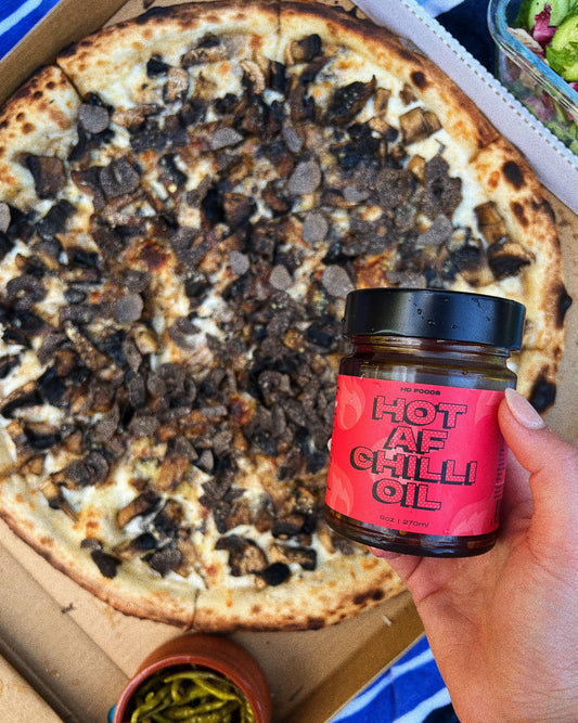 Jar of hotAF chilli oil held over a truffle mushroom pizza