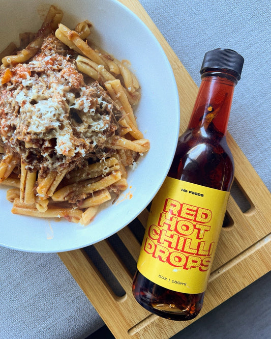 Red Hot Chilli Drops bottle next to a bowl of beef ragu pasta with parmesan