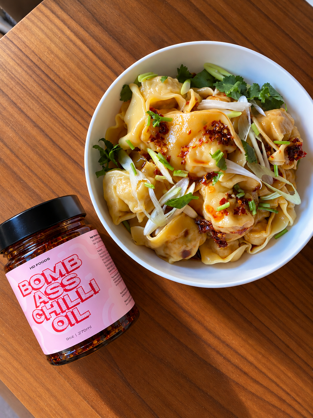 Jar of BACO chilli oil next to a bowl of wontons topped with crispy chilli oil and spring onion
