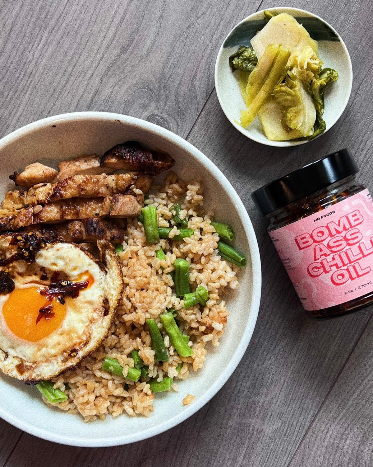 Rice bowl with grilled chicken, fried egg topped with BACO chilli oil, and a jar of BACO